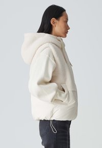 Kapuzenshirt mit einem flauschigen cremefarbenen Oberteil und einem glatten, gefütterten unteren Teil. Verfügt über Seitentaschen, einen Kordelzug am Saum und gestrickte Ärmelbündchen.