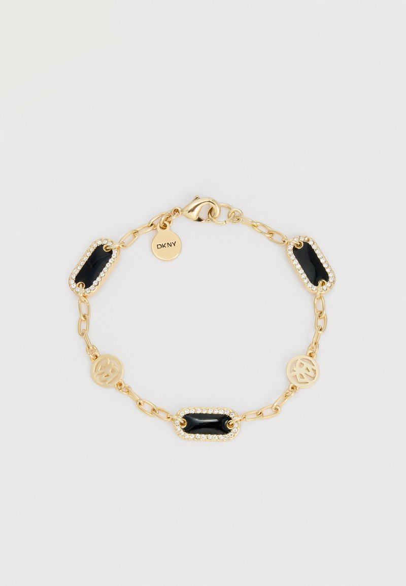 Bracelet chaîne en or avec trois rectangles en émail noir bordés de cristaux et deux breloques dorées avec le logo DKNY sur un fond clair.
