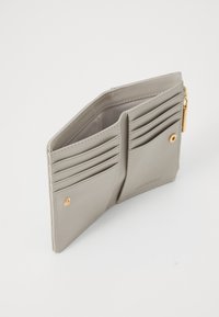 Portafoglio in pelle grigia con otto slot per carte, scomparto con zip e pulsante accentato in oro. Texture liscia e design pulito e minimalista.