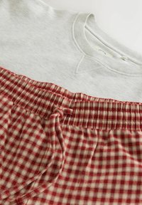 Šedá mikina s kulatým výstřihem a červené kostkované pyžamové kalhoty s elastickým pasem a šňůrkou. Měkká tkanina a pohodlný design.