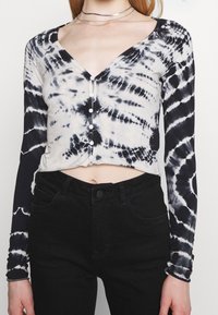 Czarny i biały crop top tie-dye z długim rękawem, dekoltem w kształcie litery V oraz zapięciem na guziki z przodu. Miękki materiał, dopasowany krój.