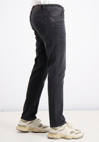 Mustad denim pahklid otse lõikega, millel on peened õmblused ja taskud. Kombineeritud heledate sportlike kingadega.