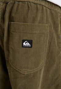 Olive green corduroy fabric with vertical stripes, featuring a patch pocket and a black Quiksilver logo tag on the side.