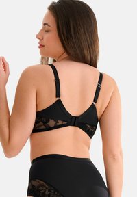 Soutien-gorge en dentelle noire au dos, avec des bretelles réglables et une fermeture crochet et œillet, mettant en valeur un tissu lisse et des détails en motif floral.