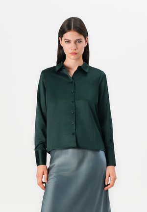 Dark green satin button-up shirt with a collar, long sleeves, and a straight hem. Paired with a smooth, shiny grey skirt.