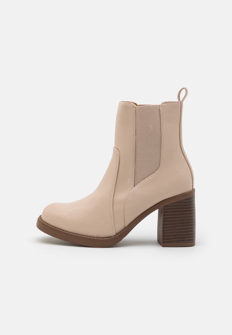 Bottines beige avec tige en cuir lisse, panneaux latéraux élastiques et talon en bois empilé. Bout arrondi et languette d'extraction.