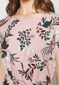 Růžová blůza s květinovými a motýlími vzory v zelené a burgundské barvě, vyrobená z lehké tkaniny, s kulatým výstřihem a krátkými rukávy.