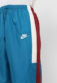 Blå Nike sportbyxor med röda och vita vertikala ränder på sidan, bärs med en vit topp.