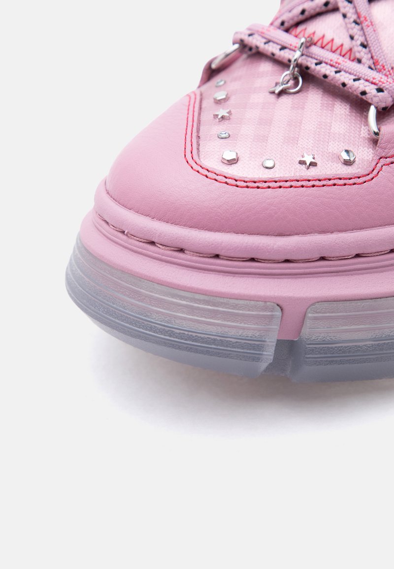 Nahaufnahme eines pinken Sneakers mit durchsichtiger Sohle, roter Naht, stern- und sternförmigen Schmucknieten sowie pinken Schnürsenkeln mit sternförmigem Anhänger.