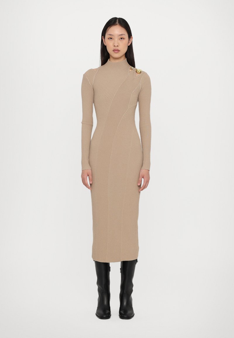 Beige ribbed knit dress with a high neckline, long sleeves, and a diagonal seam design. Features two gold accents on the shoulder.