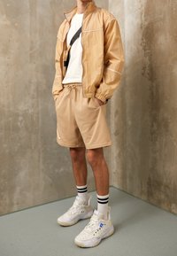 Beige lättviktsjacka med dragkedja, kombinerad med beiga shorts, vita strumpor med svarta ränder och chunky vita sneakers.