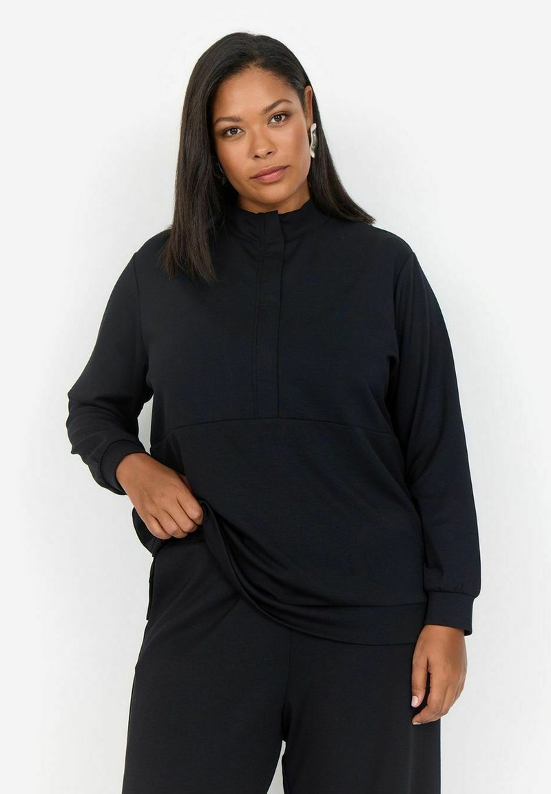 Sudadera negra con cuello alto, mangas largas y un panel frontal texturizado. Tejido suave con un corte relajado, combinado con pantalones negros a juego.