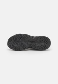 Semelle de chaussure de sport noire avec des motifs de bande de roulement texturés pour une meilleure adhérence. Présente une forme incurvée et des rainures prononcées pour une traction améliorée.