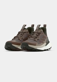 Pruunid spordijalatsid, mis on tehtud siledate ja tekstuursete materjalide segust, paksu valge keskosaga, musta tallaga ja helendavate detailidega.