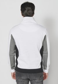Felpa da uomo con collo alto, caratterizzata da un corpo bianco, pannelli laterali grigi e neri e polsini a coste. Tessuto con texture liscia.