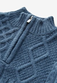 Maglione blu lavorato a maglia con colletto alto, caratterizzato da un motivo a diamante testurizzato e un dettaglio con zip argentata sul collo.