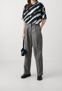 Camiseta de gran tamaño en blanco y negro con efecto tie-dye, combinada con pantalones gris de talle alto con pliegues; el modelo sostiene un pequeño bolso negro.