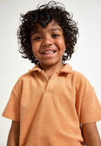 Kortærmet polo t-shirt med krave i blød, struktureret ferskenfarvet stof, med en halv-knapneplacket og afslappet pasform. Barn smiler.