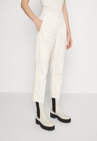 Persoon in hoge taille witte crop pants met elastische achterkant en witte plateau laarzen met zwarte elastische zijpanelen.