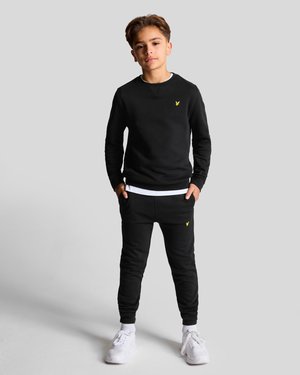Sweatshirt noir et joggeurs avec des poignets côtelés et une bande blanche. Détail du logo jaune sur la poitrine et la hanche. Baskets blanches. Texture lisse.
