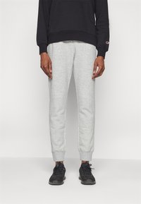 Szürke, szűkített lábú melegítőnadrág, puha anyagból. Gumis derékrész és mandzsetta, fekete kapucnis sweatshirt-tel és fekete sportcipővel párosítva.