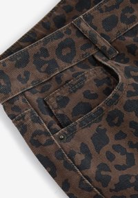 Materijal u leopard uzorku, smeđi kord od samta s crnim mrljama. Ima stražnji džep s metalnim zatvaračem i vidljivim šavovima.