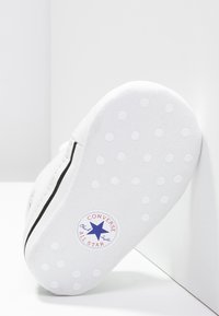 Białe sneakersy z teksturowanym płótnem, czarnym wykończeniem i kropkowaną gumową podeszwą. Posiadają niebieskie logo w kształcie gwiazdy oraz branding "CONVERSE ALL STAR".