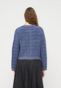 Μπλε πλ εκτό πουλόβερ με υφή και ριμπ μανσέτες, με κομμένο σχέδιο και στρογγυλή λαιμόκοψη. Φορεμένο με μαύρη πλισέ φούστα.