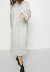 Vestido sudadera gris de manga larga, hecho de una tela suave. Presenta un corte holgado, escote redondo y puños acanalados, llegando hasta la mitad de la pantorrilla.