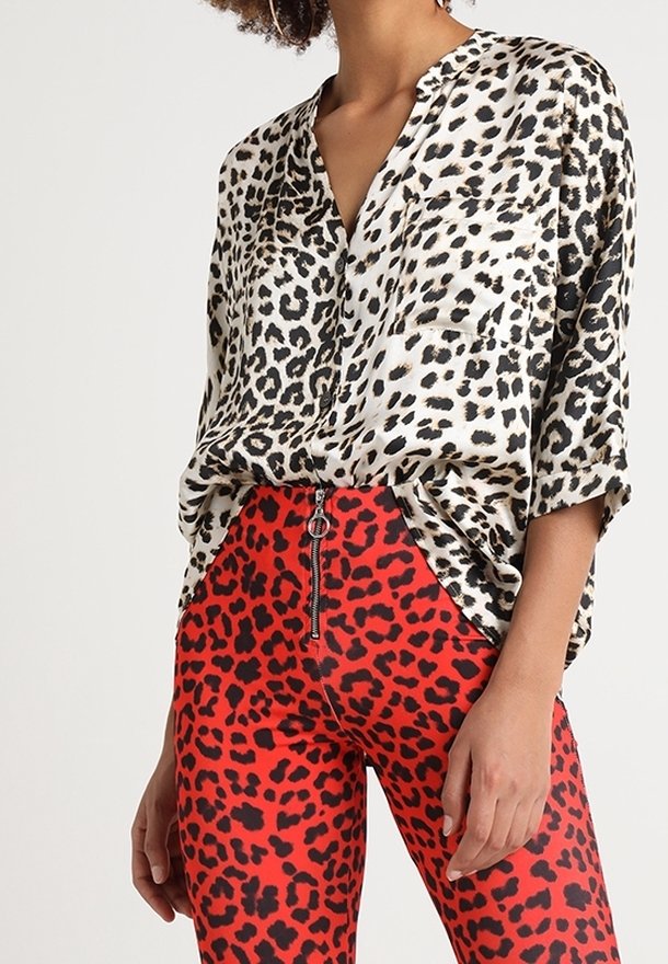 Leopardmönstrad silkesblus med V-hals och korta ärmar, tillsammans med röda leggings med ett svart leopardmönster och framfickor.