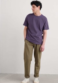Fialové bavlněné tričko s krátkým rukávem, spárované s olivově zelenými kalhotami a bílými teniskami. Oblečení spojuje ležérní střih a pohodlí.