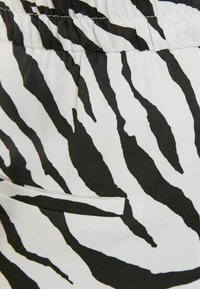 Černobílá látka se zebřími pruhy, s elastickým pasem a drobným detailem kapsy. Hladká textura a výrazný vzor.