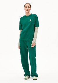 Grünes Baumwoll-T-Shirt und Hosen-Set. Das T-Shirt verfügt über ein Logo aus weißem Band, lockere Passform. Glatte Textur, lange Ärmel darunter.