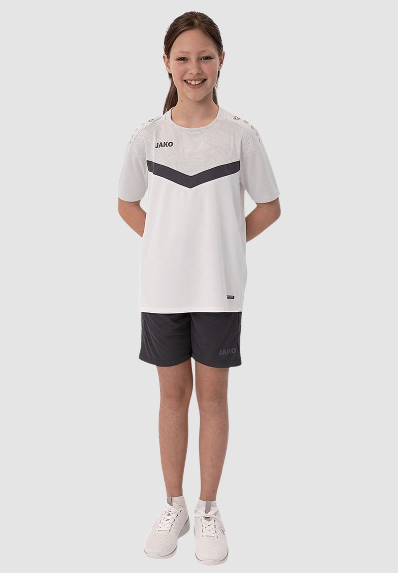 Witte sportshirt met grijze accenten en logo, gecombineerd met grijze shorts, gedragen met witte sneakers. De outfit is geschikt voor sportactiviteiten.