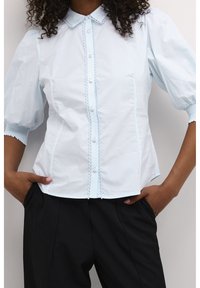 Light blue short-sleeve blouse with a scalloped collar, button-down front, and textured detailing along the seams. Tailored fit, cotton fabric.