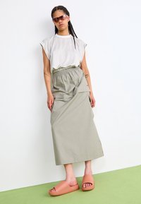 Light gray, short-sleeved top with subtle stripes; olive green, wrap-style skirt with an elastic waistband; pale orange slide sandals.