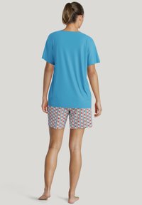 Blauw T-shirt met korte mouwen en een relaxte pasvorm, gecombineerd met een short met een patroon van rode bloemen op een gestreepte achtergrond.