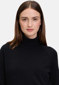 Schwarzer Rollkragenpullover mit weicher Textur, raglanärmeln und schmalem Kragen. Einfaches, sauberes Design ohne Verzierungen.