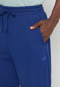 Granatowe spodnie dresowe z miękkiej bawełny; posiadają elastyczny pasek w talii z sznurkiem i boczne kieszenie. Logo nadrukowane na nodze.