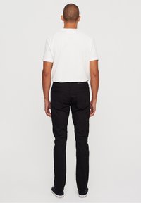 Svarta denimjeans med slim fit och två bakfickor, kombinerat med en vit kortärmad skjorta och svarta sneakers. Enkelt mönster, inga tryck.