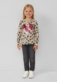  Lange mouwen beige top met zwart en roze luipaardprint, met een glanzend roze pailletten hart. Gecombineerd met donkere jeans en witte sneakers.