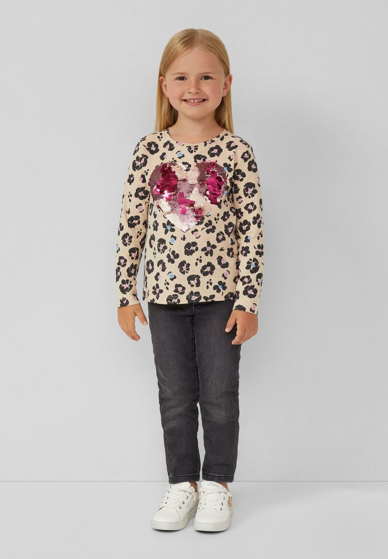  Lange mouwen beige top met zwart en roze luipaardprint, met een glanzend roze pailletten hart. Gecombineerd met donkere jeans en witte sneakers.