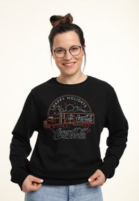 Felpa nera con una grafica natalizia colorata della Coca-Cola che presenta un camion, montagne ed elementi festivi. Vestibilità comoda e maniche lunghe.