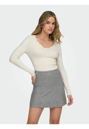 Rebrasta kremasta majica s izrezom na rubu i dugim rukavima, u kombinaciji sa sivom suknjom koja ima glatku teksturu i detalje na pojasu.