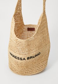 Geantă din paie țesută, de culoare bej natural, cu un deschidere spațioasă și logo-ul „VANESSA BRUNO” în culoare neagră. Include o etichetă din piele netedă în interior.