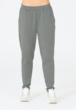 Grå avsmalnande joggingbyxor gjorda av mjukt tyg, med elastisk midja och sidofickor, tillsammans med vita sportiga sneakers.