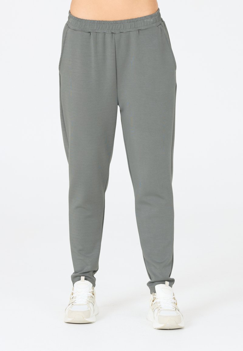 Grå avsmalnande joggingbyxor gjorda av mjukt tyg, med elastisk midja och sidofickor, tillsammans med vita sportiga sneakers.