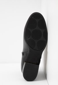 Semelle de botte en cuir noir avec des motifs circulaires de bande de roulement, taille 37 marquée, et un talon bloc sur fond blanc.