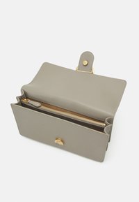 Pelēka ādas soma ar atloku aizdari un zelta toņa aparatūru. Iespējama ar rāvējslēdzēja nodalījumu un divām atvērtām sekcijām iekšpusē. Gluda tekstūra.