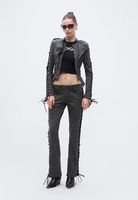 Hall hall teksariidest jakk pits-up detailidega, sobitatud sama värvi hallide pükstega, millel on külgpitsid, täiustatud mustade kontsadega saapade ja päikeseprillidega.